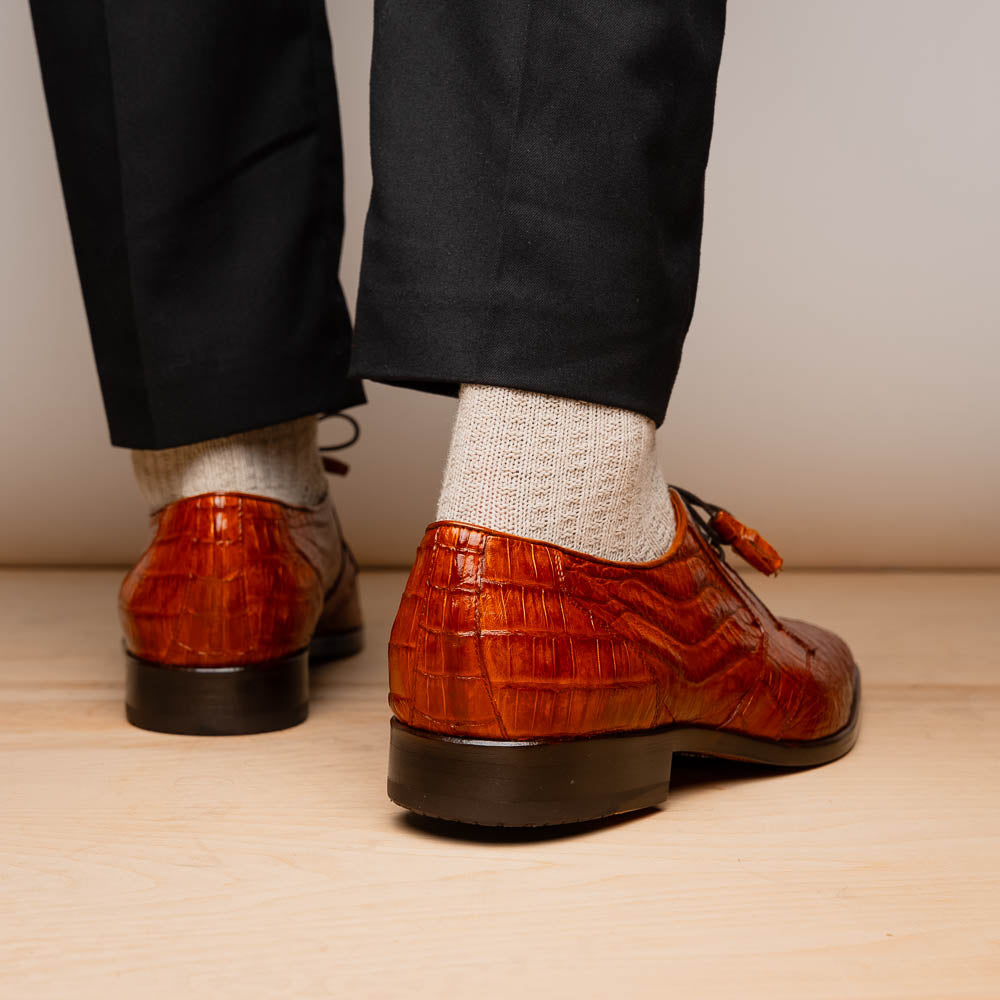 A pair of Marco Di Milano Lacio Brandy luxury derby shoes in a brown crocodile pattern, crafted from genuine caiman leather—one upright and one on its side to highlight the signature sole branding.