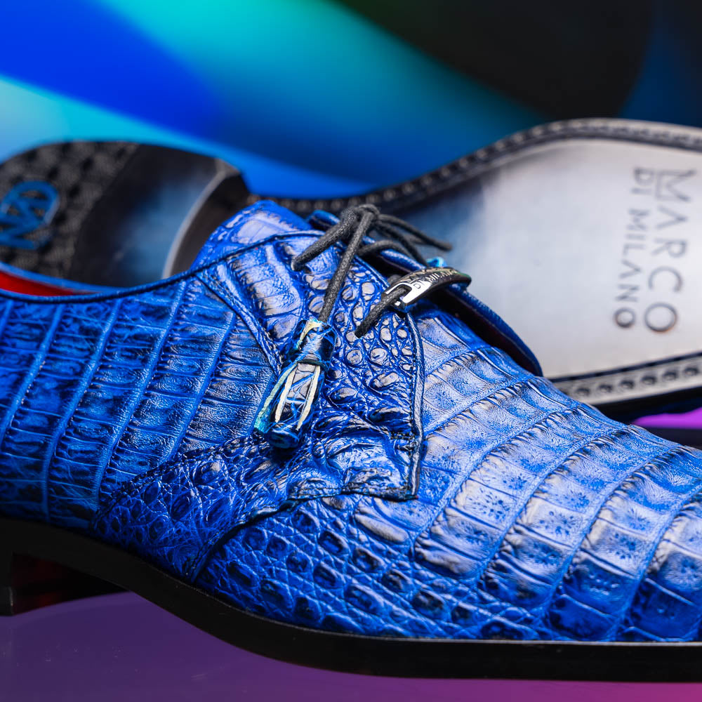 Marco Di Milano’s Lacio Electric Blue men’s dress shoes feature genuine caiman crocodile leather in blue, black laces, a bold red interior, with one shoe standing upright and the other lying on its side.