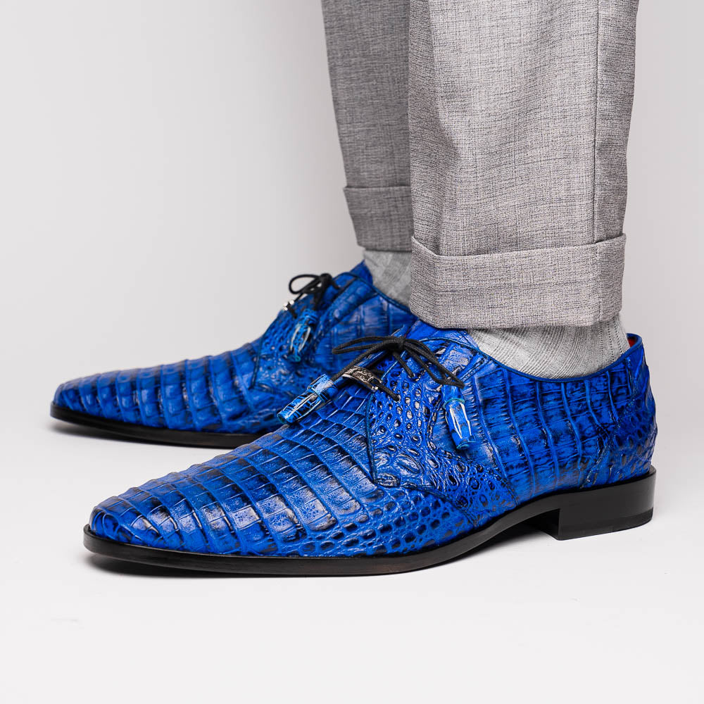 Marco Di Milano’s Lacio Electric Blue men’s dress shoes feature genuine caiman crocodile leather in blue, black laces, a bold red interior, with one shoe standing upright and the other lying on its side.