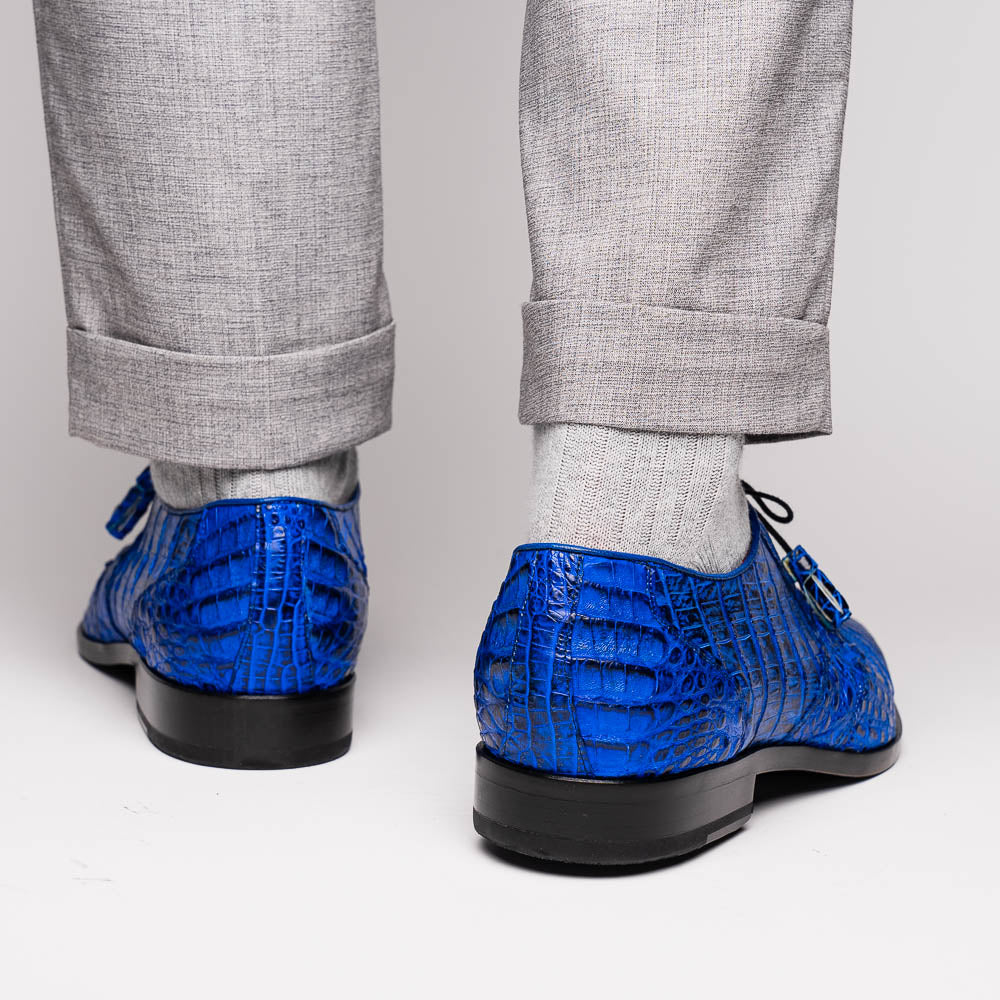 Marco Di Milano’s Lacio Electric Blue men’s dress shoes feature genuine caiman crocodile leather in blue, black laces, a bold red interior, with one shoe standing upright and the other lying on its side.