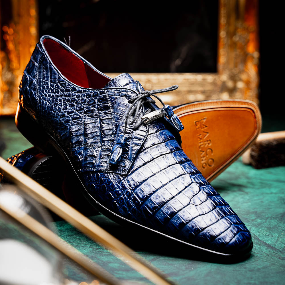 The Lacio Navy by Marco Di Milano are luxury dress derby shoes made from genuine caiman crocodile leather, featuring elegant tassels, a red interior lining, and tan leather soles stamped with the brand’s name.