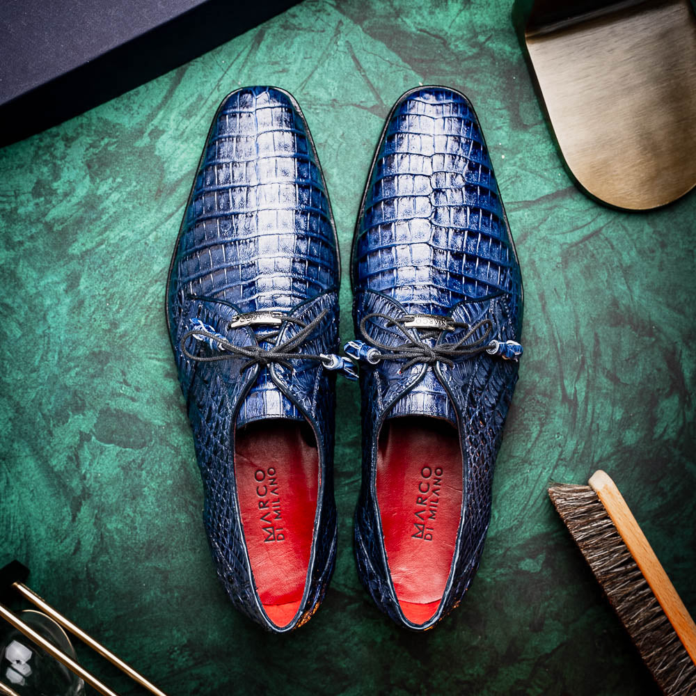 The Lacio Navy by Marco Di Milano are luxury dress derby shoes made from genuine caiman crocodile leather, featuring elegant tassels, a red interior lining, and tan leather soles stamped with the brand’s name.