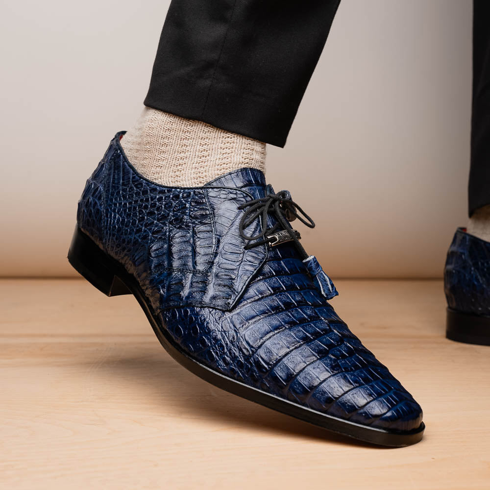 The Lacio Navy by Marco Di Milano are luxury dress derby shoes made from genuine caiman crocodile leather, featuring elegant tassels, a red interior lining, and tan leather soles stamped with the brand’s name.