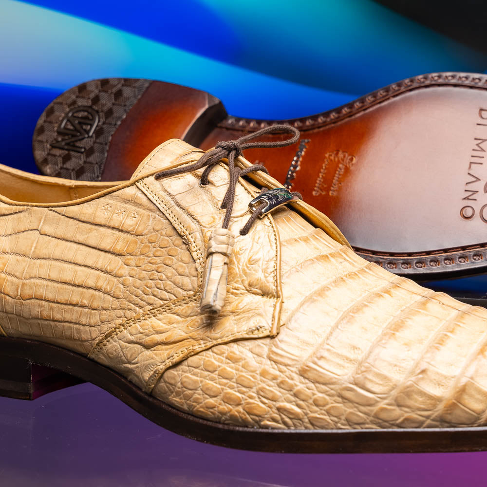 A pair of beige Marco Di Milano Lacio Orix shoes in genuine caiman crocodile, featuring a luxury derby design with dark brown laces—one upright, the other on its side to display the detailed sole.