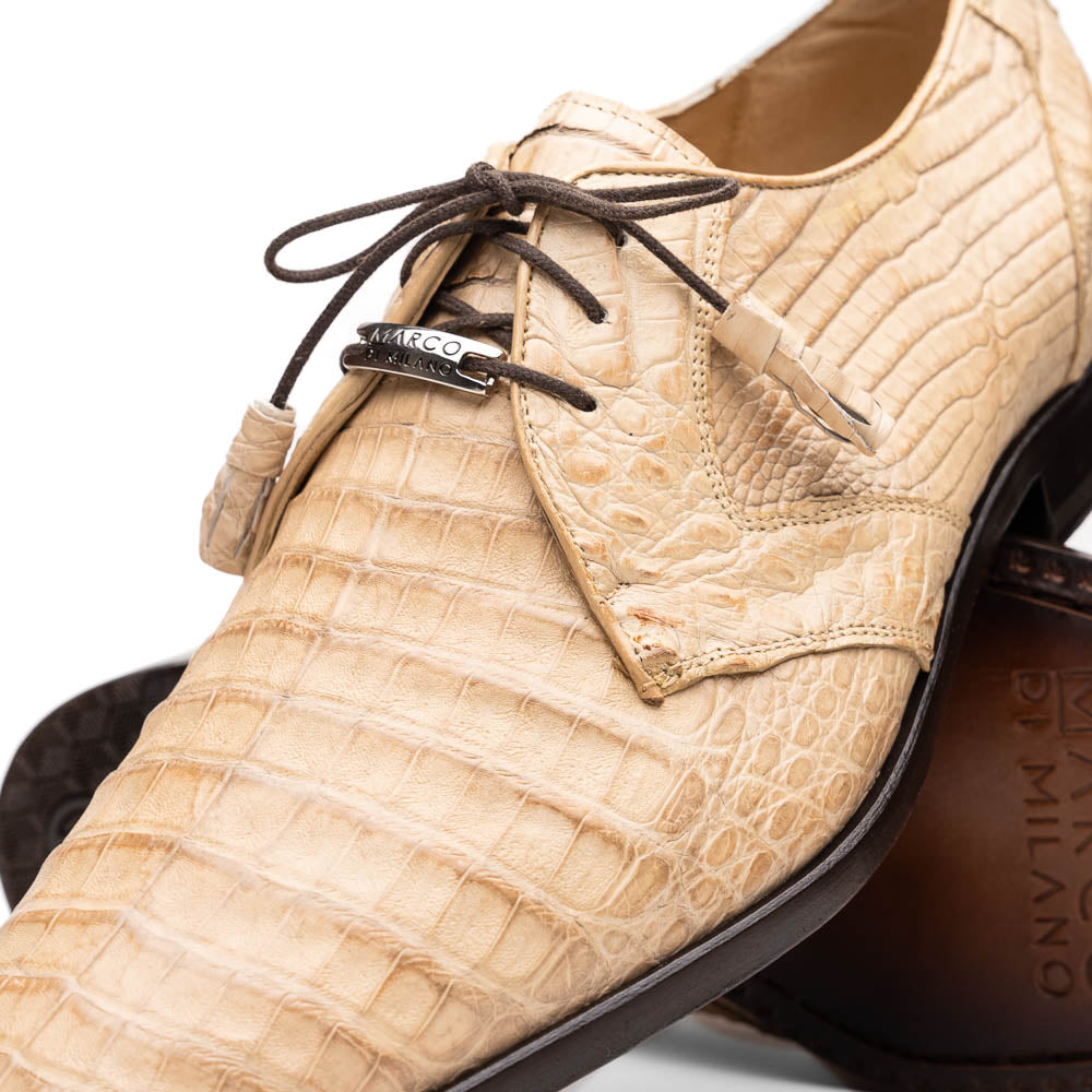 A pair of beige Marco Di Milano Lacio Orix shoes in genuine caiman crocodile, featuring a luxury derby design with dark brown laces—one upright, the other on its side to display the detailed sole.