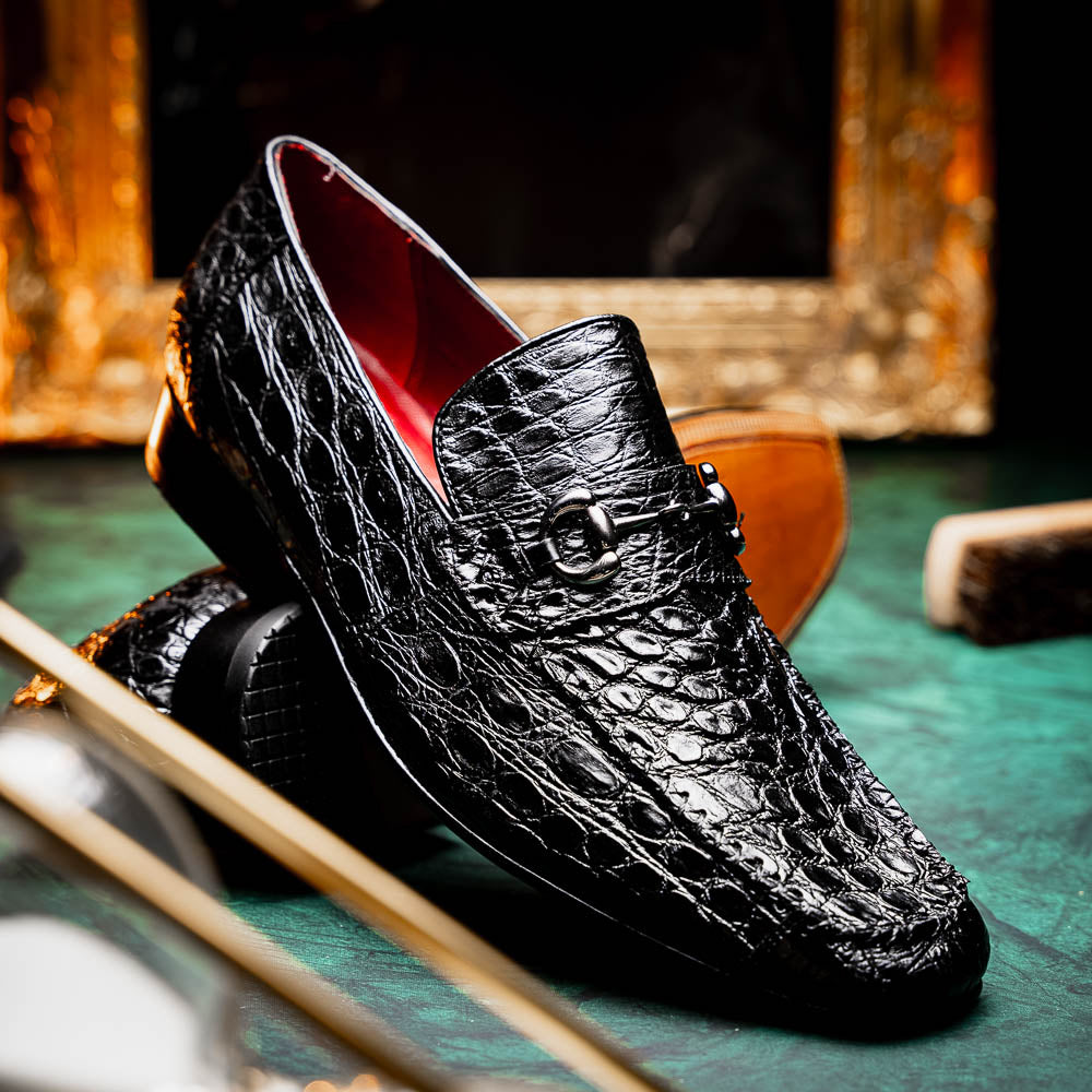 A pair of Marco Di Milano Landro Black crocodile-pattern luxury loafers with metal bit detail: one shoe stands upright, the other lies on its side displaying the tan sole labeled "Marco Di Milano.