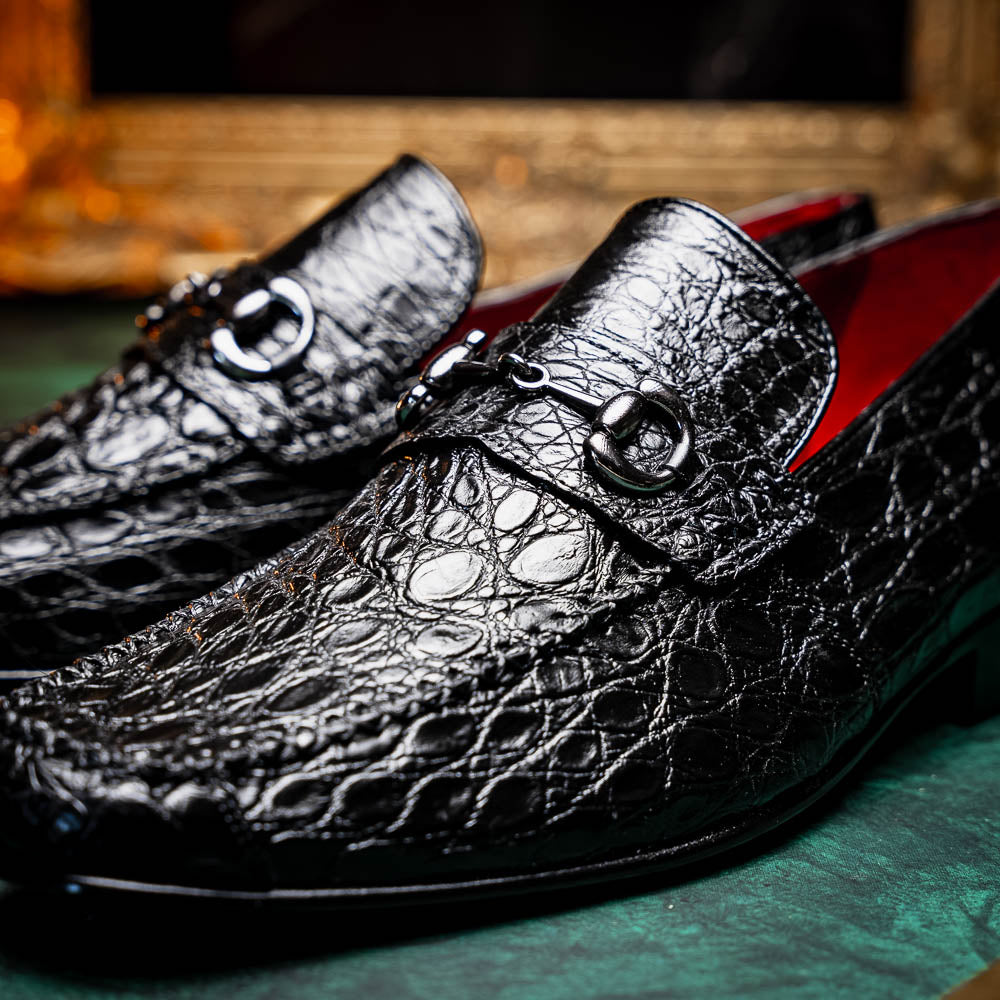 A pair of Marco Di Milano Landro Black crocodile-pattern luxury loafers with metal bit detail: one shoe stands upright, the other lies on its side displaying the tan sole labeled "Marco Di Milano.