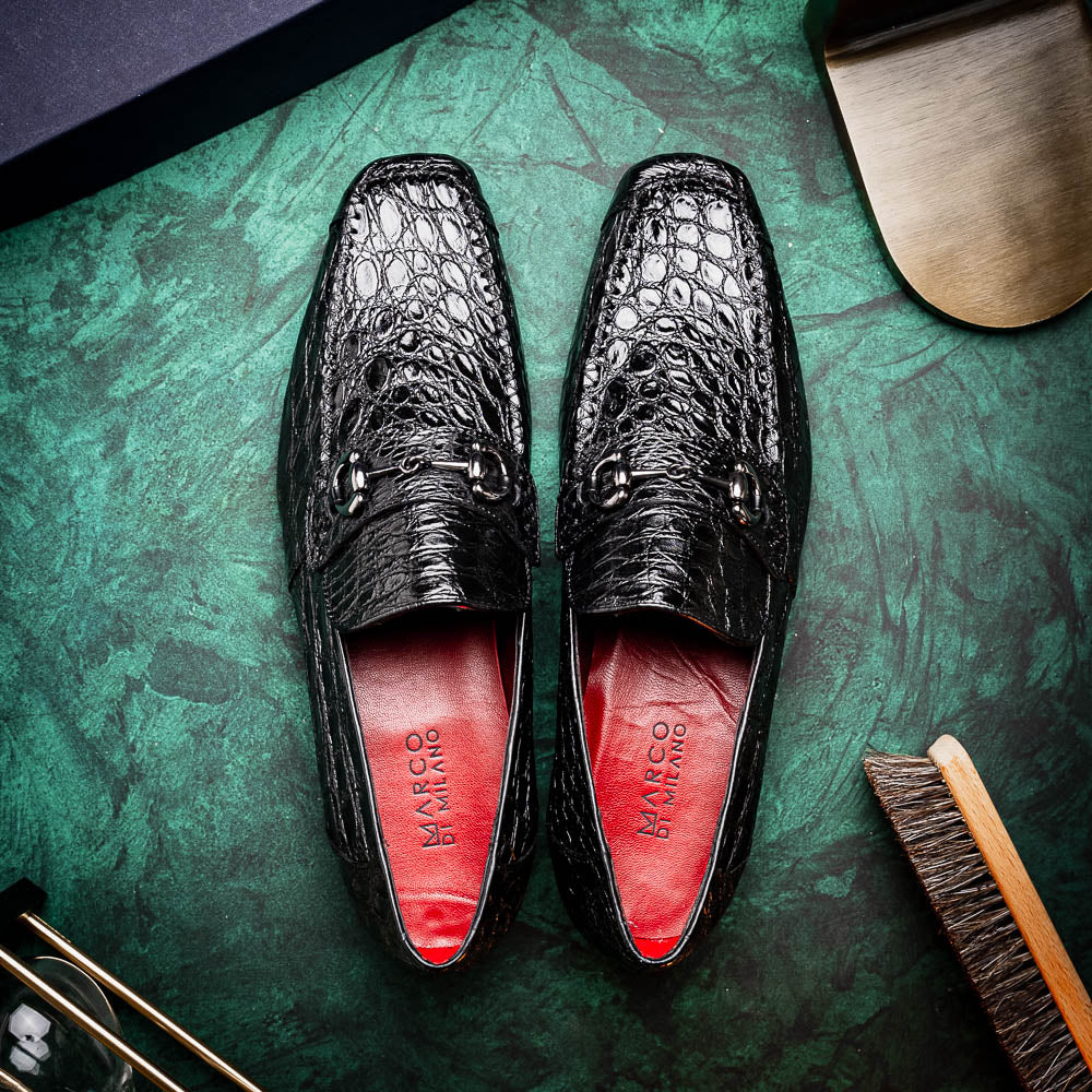 A pair of Marco Di Milano Landro Black crocodile-pattern luxury loafers with metal bit detail: one shoe stands upright, the other lies on its side displaying the tan sole labeled "Marco Di Milano.