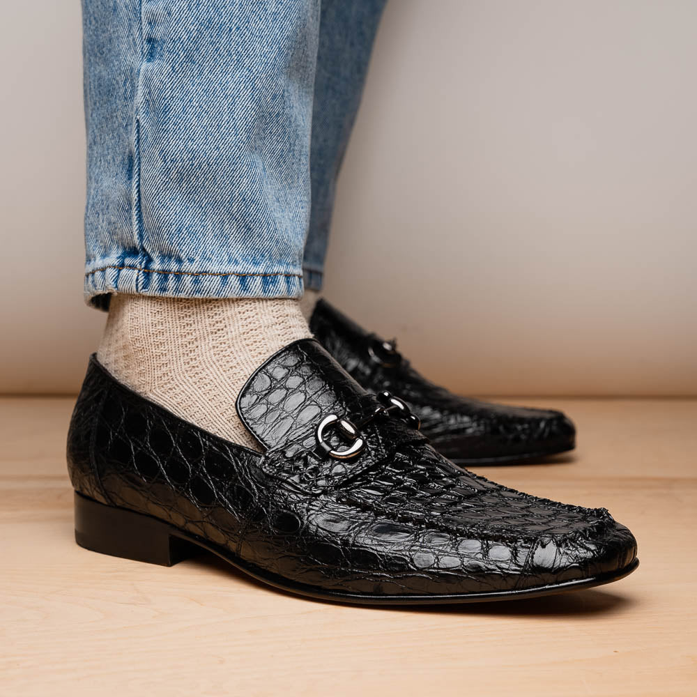 A pair of Marco Di Milano Landro Black crocodile-pattern luxury loafers with metal bit detail: one shoe stands upright, the other lies on its side displaying the tan sole labeled "Marco Di Milano.