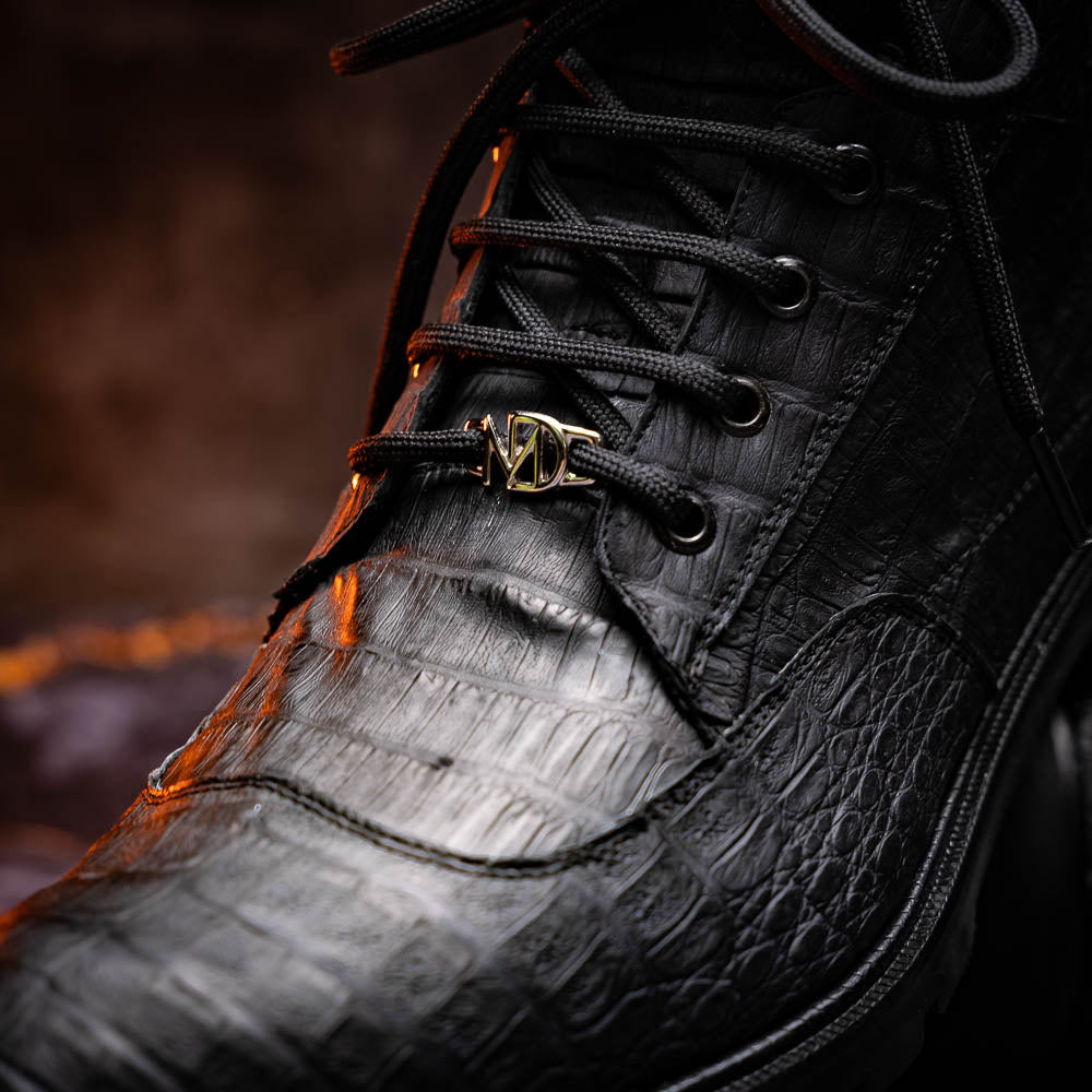 The Leoni Oil Black boots by Marco Di Milano feature genuine caiman leather in a crocodile texture, black laces, and rugged rubber soles—luxurious footwear with striking details.