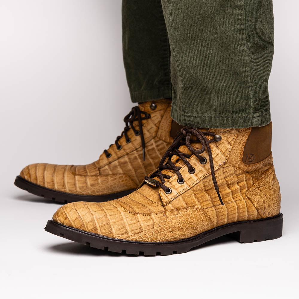 The Leoni Oil Orix by Marco Di Milano features tan crocodile-patterned leather lace-up boots with brown rubber soles, showcased upright and sideways to highlight the tread—a refined choice in luxury men's footwear.
