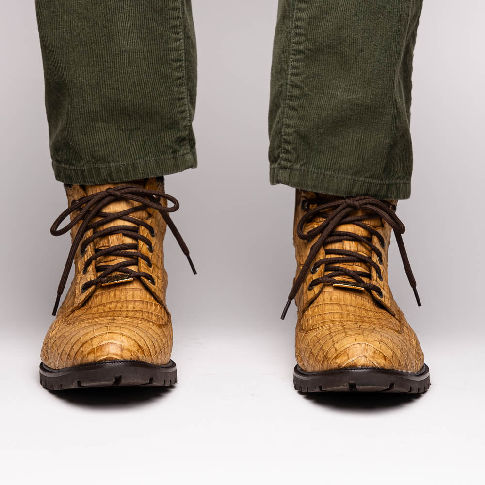 The Leoni Oil Orix by Marco Di Milano features tan crocodile-patterned leather lace-up boots with brown rubber soles, showcased upright and sideways to highlight the tread—a refined choice in luxury men's footwear.