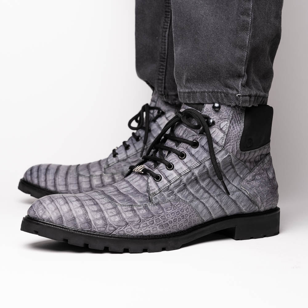 The Leoni Oil Gray boot by Marco Di Milano features a gray, crocodile-patterned design in genuine caiman leather with black laces, a thick rugged sole, and hand-painted finishes—all showcased on a white background.