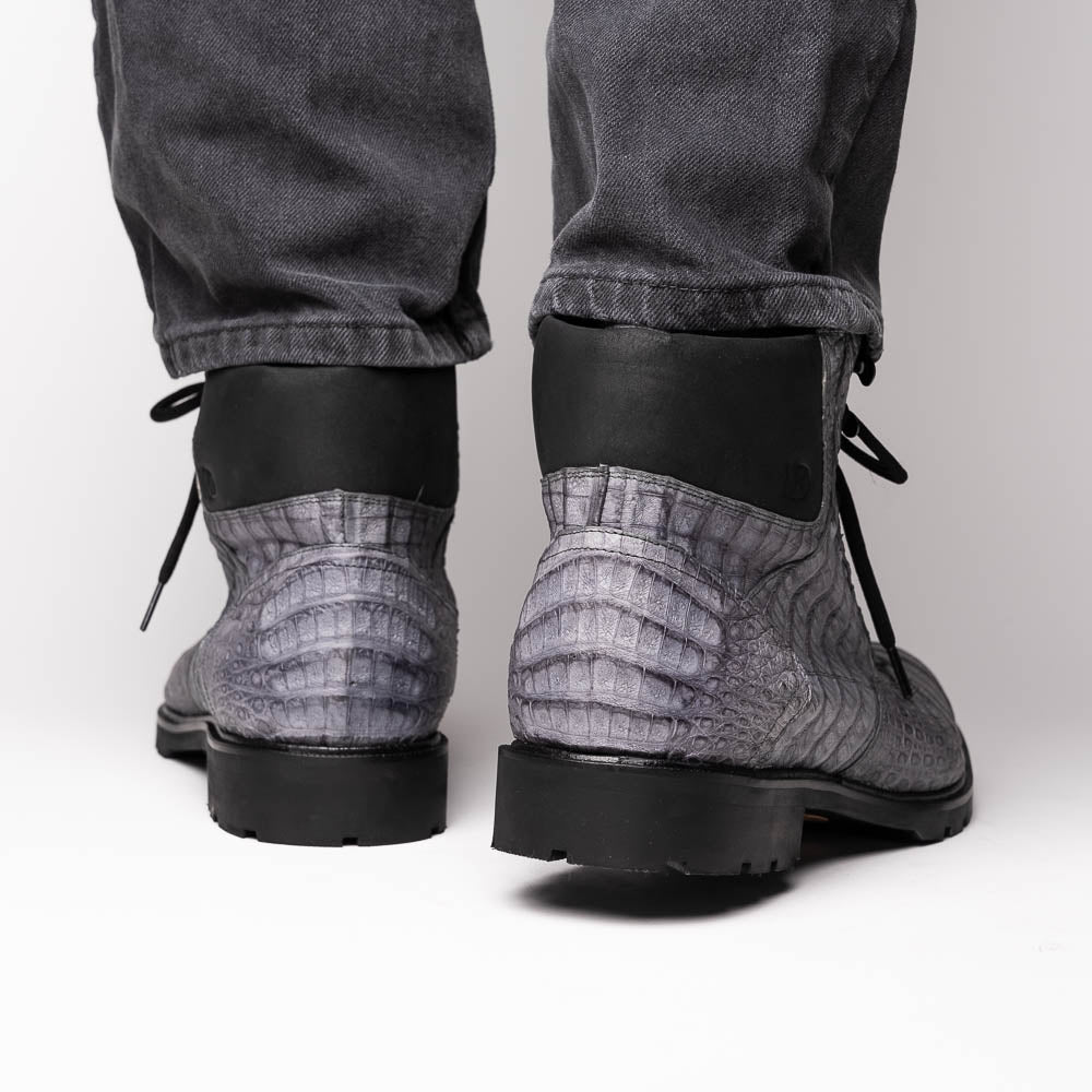 The Leoni Oil Gray boot by Marco Di Milano features a gray, crocodile-patterned design in genuine caiman leather with black laces, a thick rugged sole, and hand-painted finishes—all showcased on a white background.