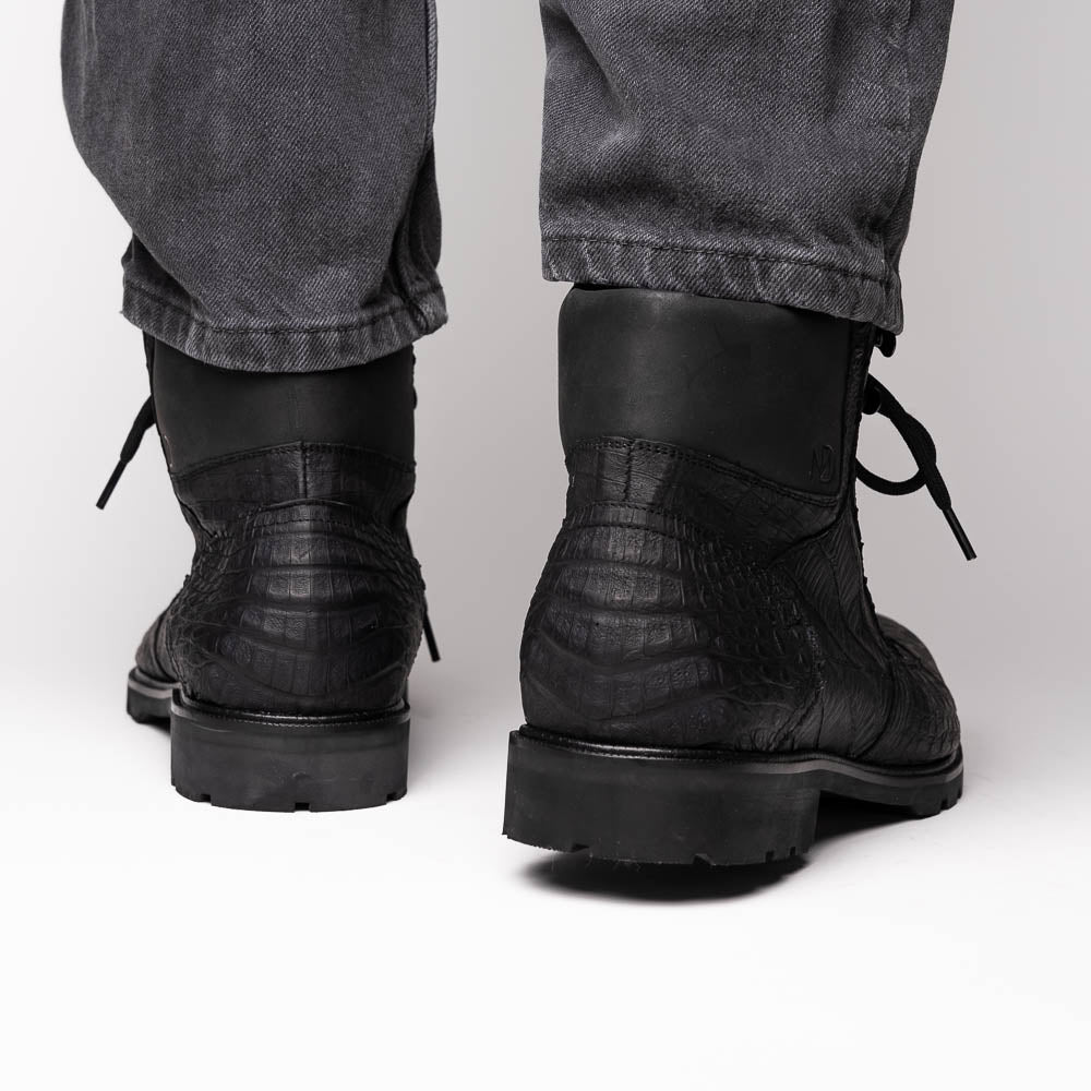 The Leoni Oil Black boots by Marco Di Milano feature genuine caiman leather in a crocodile texture, black laces, and rugged rubber soles—luxurious footwear with striking details.
