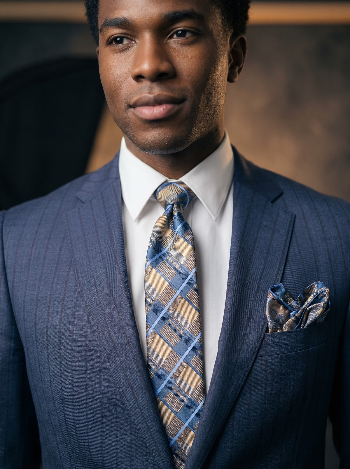 A man wearing a Tiglio Luxe Dolcetto Modern Fit Wool Suit TL8092 Navy/Black Pinstripe, a white dress shirt, and a blue and tan plaid tie with a matching pocket square.