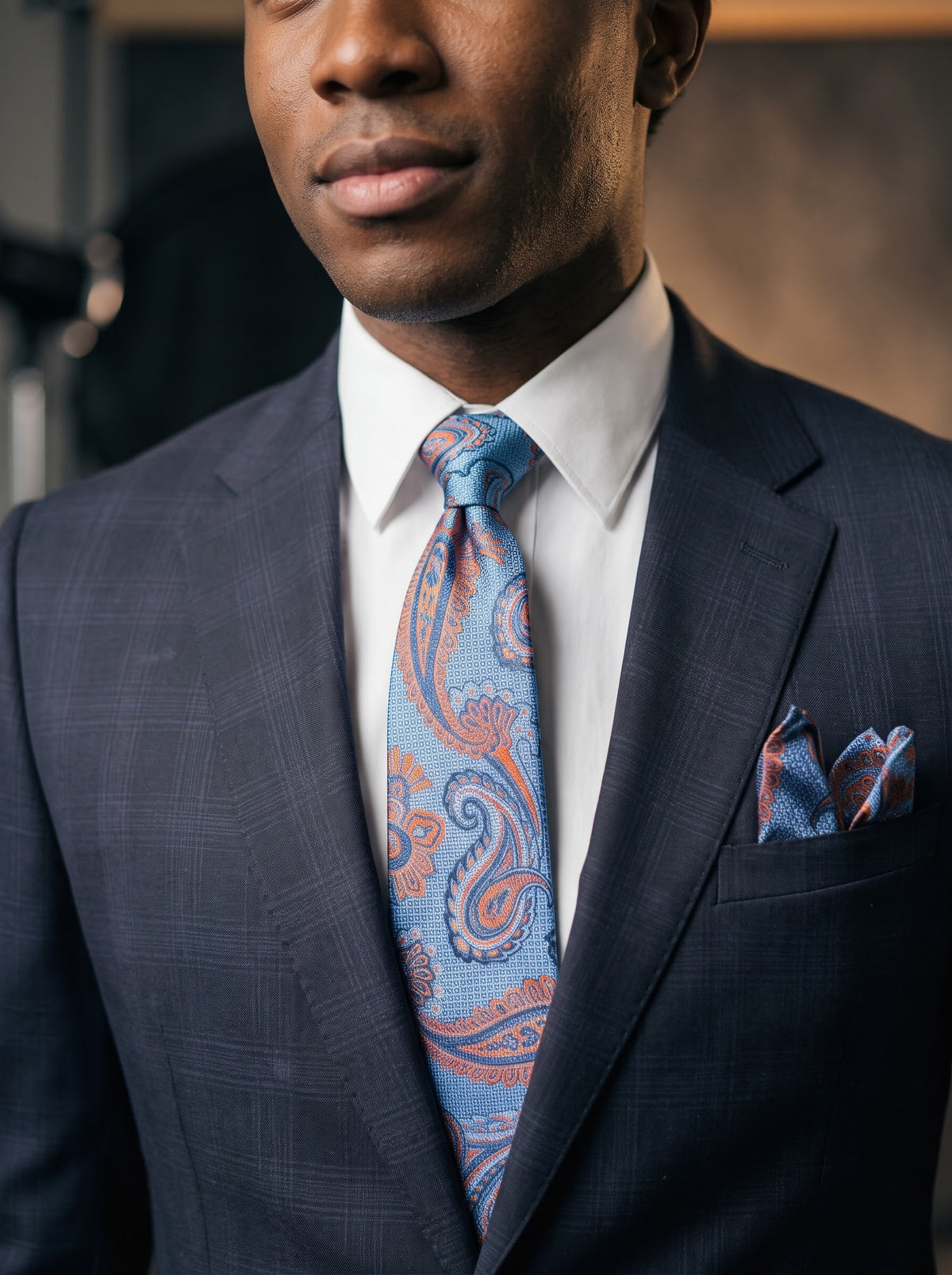 A man wears a Tiglio Luxe Capri Modern Fit Wool Suit WS8502 Navy Plaid, styled with a white shirt, paisley tie, and pocket square.