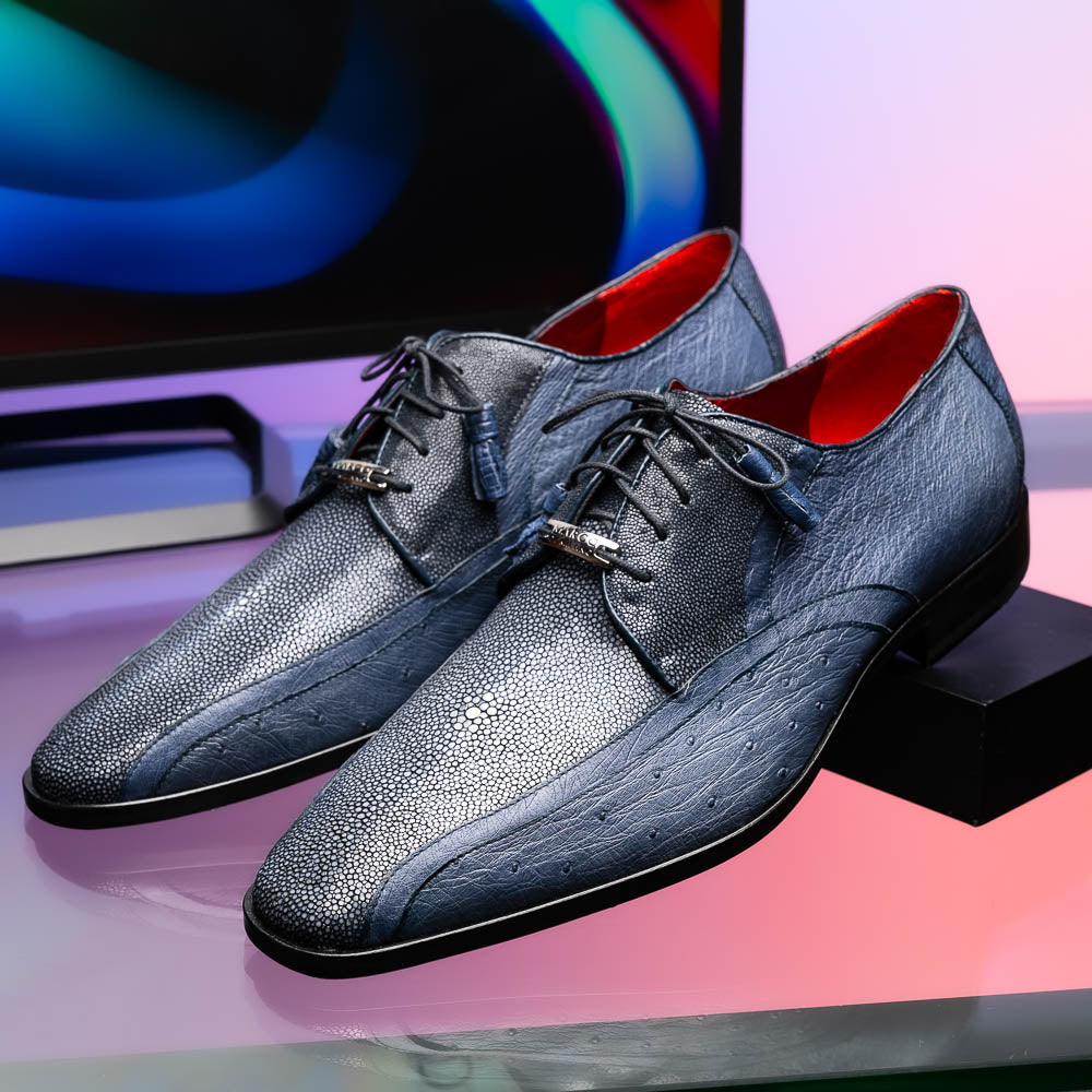 The Lucca Navy by Marco Di Milano: dark blue ostrich dress derby shoes with black soles, lace-up closures, and a textured finish. One shoe stands upright while the other lays on its side, highlighting hand-painted details.