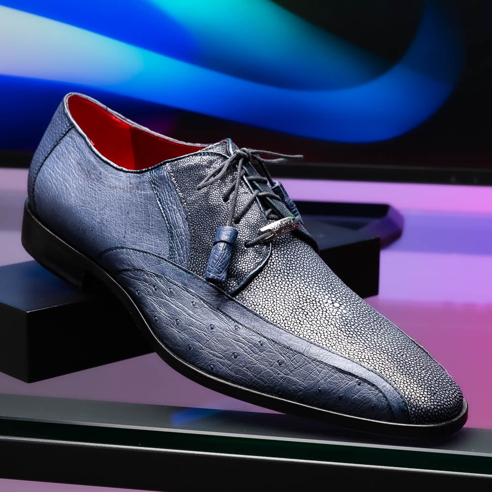 The Lucca Navy by Marco Di Milano: dark blue ostrich dress derby shoes with black soles, lace-up closures, and a textured finish. One shoe stands upright while the other lays on its side, highlighting hand-painted details.