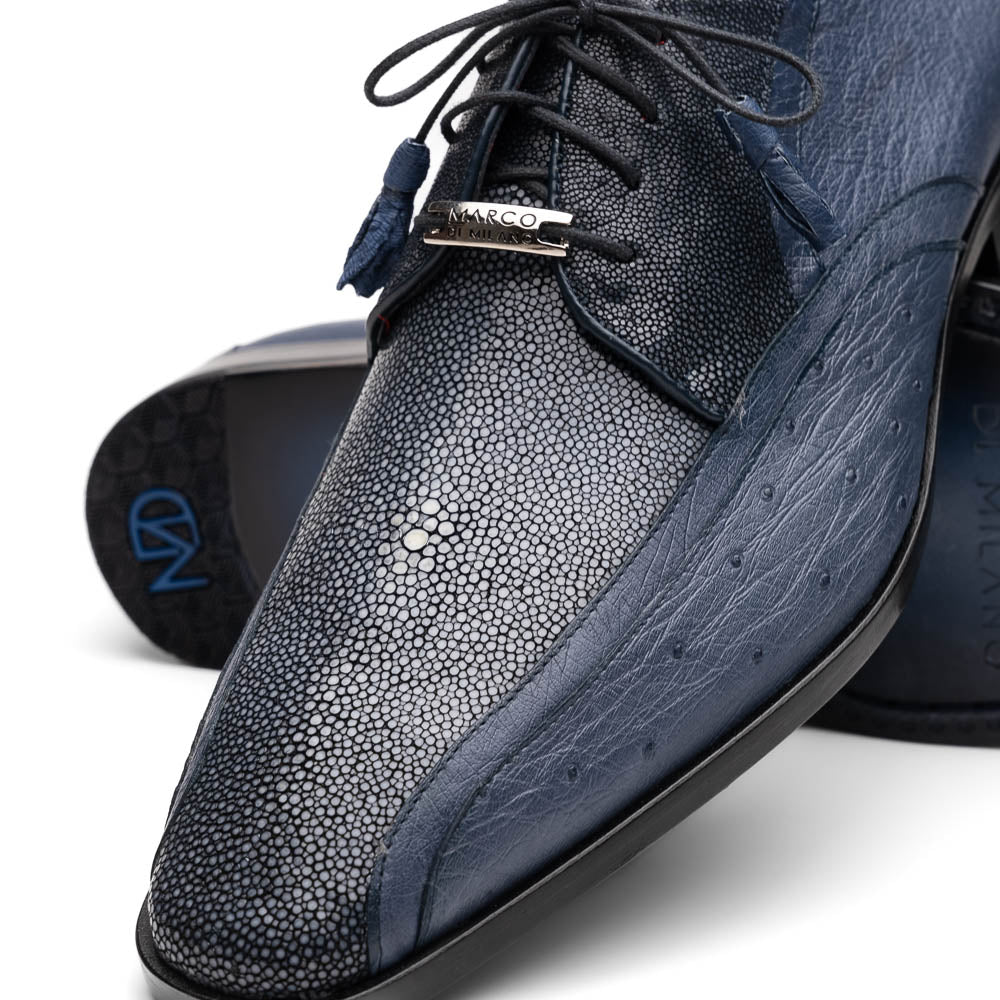 The Lucca Navy by Marco Di Milano: dark blue ostrich dress derby shoes with black soles, lace-up closures, and a textured finish. One shoe stands upright while the other lays on its side, highlighting hand-painted details.