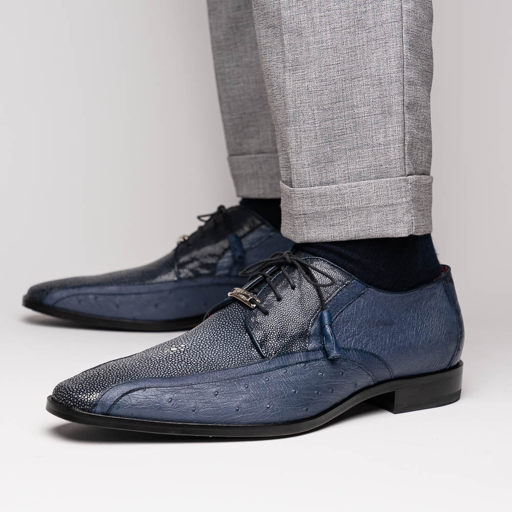 The Lucca Navy by Marco Di Milano: dark blue ostrich dress derby shoes with black soles, lace-up closures, and a textured finish. One shoe stands upright while the other lays on its side, highlighting hand-painted details.