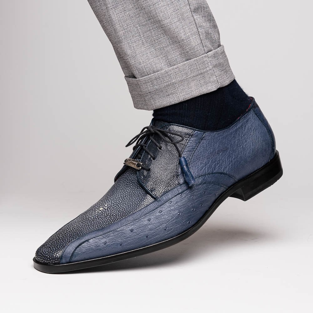 The Lucca Navy by Marco Di Milano: dark blue ostrich dress derby shoes with black soles, lace-up closures, and a textured finish. One shoe stands upright while the other lays on its side, highlighting hand-painted details.