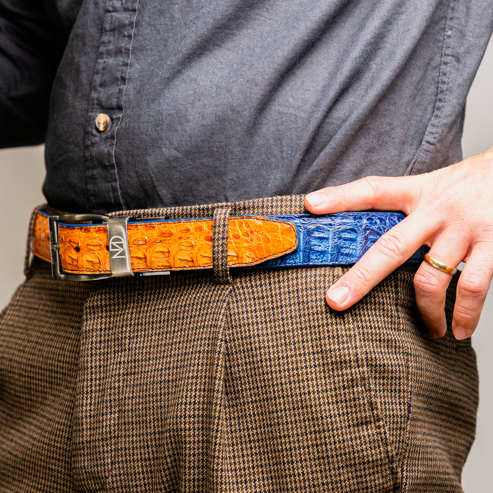 The Luciano Belt in Blue and Brandy by Marco Di Milano—both crafted from genuine caiman leather and adorned with silver buckles—are elegantly coiled together against a white background.