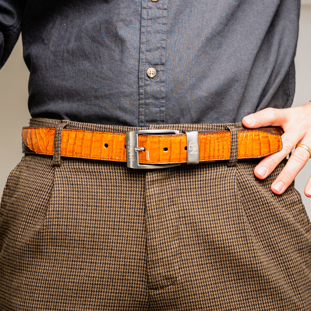 Two handcrafted men’s belts from Marco Di Milano—the Luciano Belt in Brown and Cognac—are coiled and stacked, each highlighted by a silver buckle. These premium accessories showcase the refined elegance and distinctive character of genuine caiman leather, perfect for those who value superior quality.