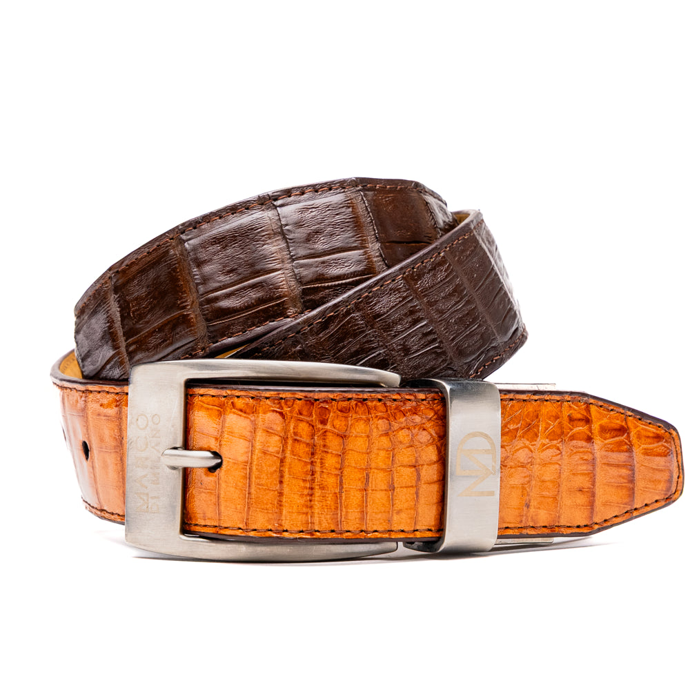 Two handcrafted men’s belts from Marco Di Milano—the Luciano Belt in Brown and Cognac—are coiled and stacked, each highlighted by a silver buckle. These premium accessories showcase the refined elegance and distinctive character of genuine caiman leather, perfect for those who value superior quality.