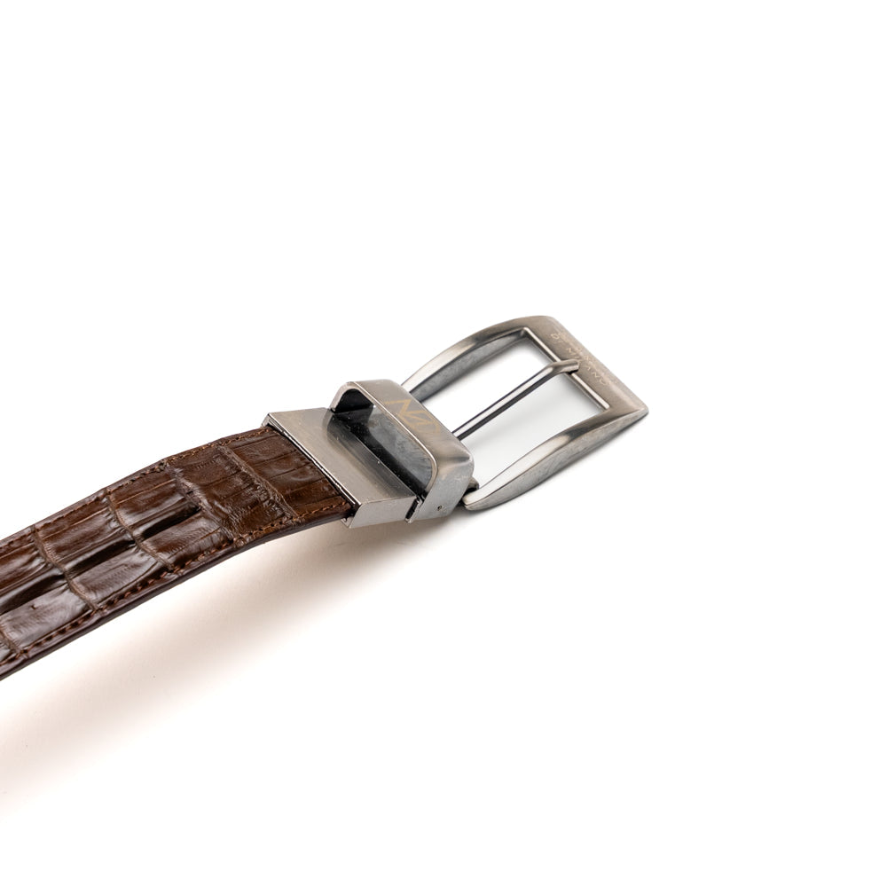 Two handcrafted men’s belts from Marco Di Milano—the Luciano Belt in Brown and Cognac—are coiled and stacked, each highlighted by a silver buckle. These premium accessories showcase the refined elegance and distinctive character of genuine caiman leather, perfect for those who value superior quality.