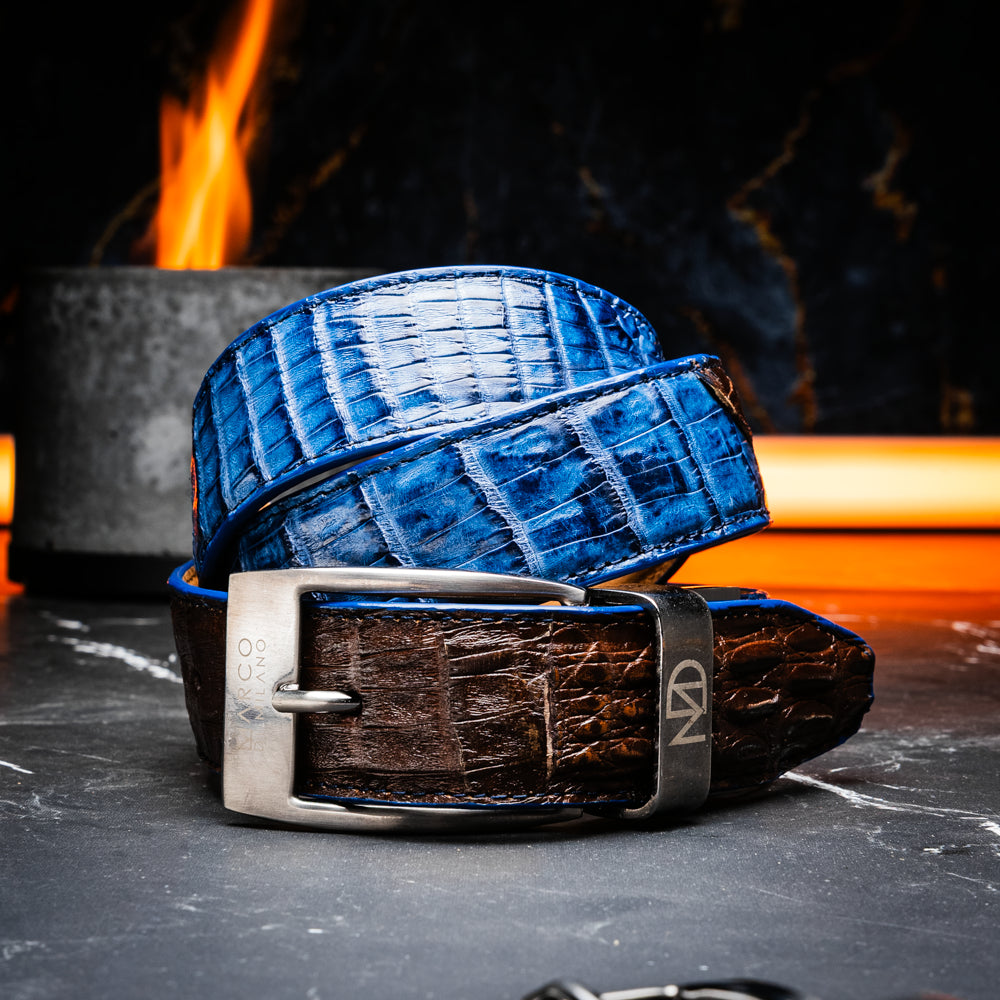 Introducing the Luciano Belt Navy / Brown by Marco Di Milano, a handcrafted luxury belt featuring an exotic crocodile-patterned leather in striking blue and dark brown sections with a refined silver buckle, elegantly coiled on a white background.