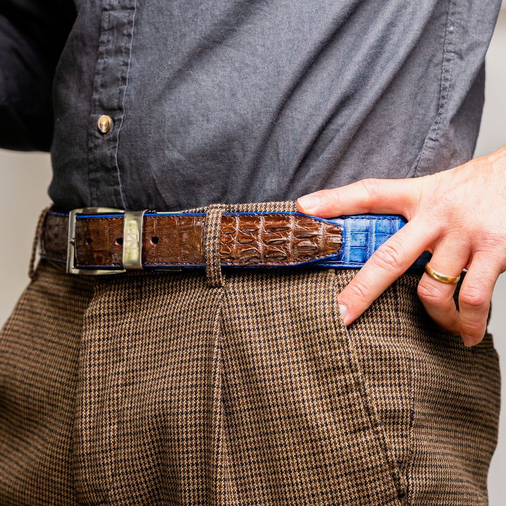 Introducing the Luciano Belt Navy / Brown by Marco Di Milano, a handcrafted luxury belt featuring an exotic crocodile-patterned leather in striking blue and dark brown sections with a refined silver buckle, elegantly coiled on a white background.