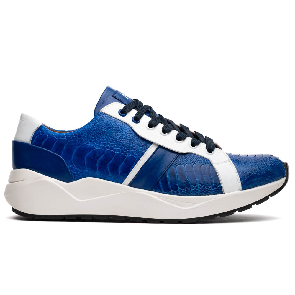The Marco Di Milano Lyon Blue / White sneakers feature blue and white tones, black laces, textured side panels, and sleek black outsoles, with one shoe displayed stylishly on its side against the other.
