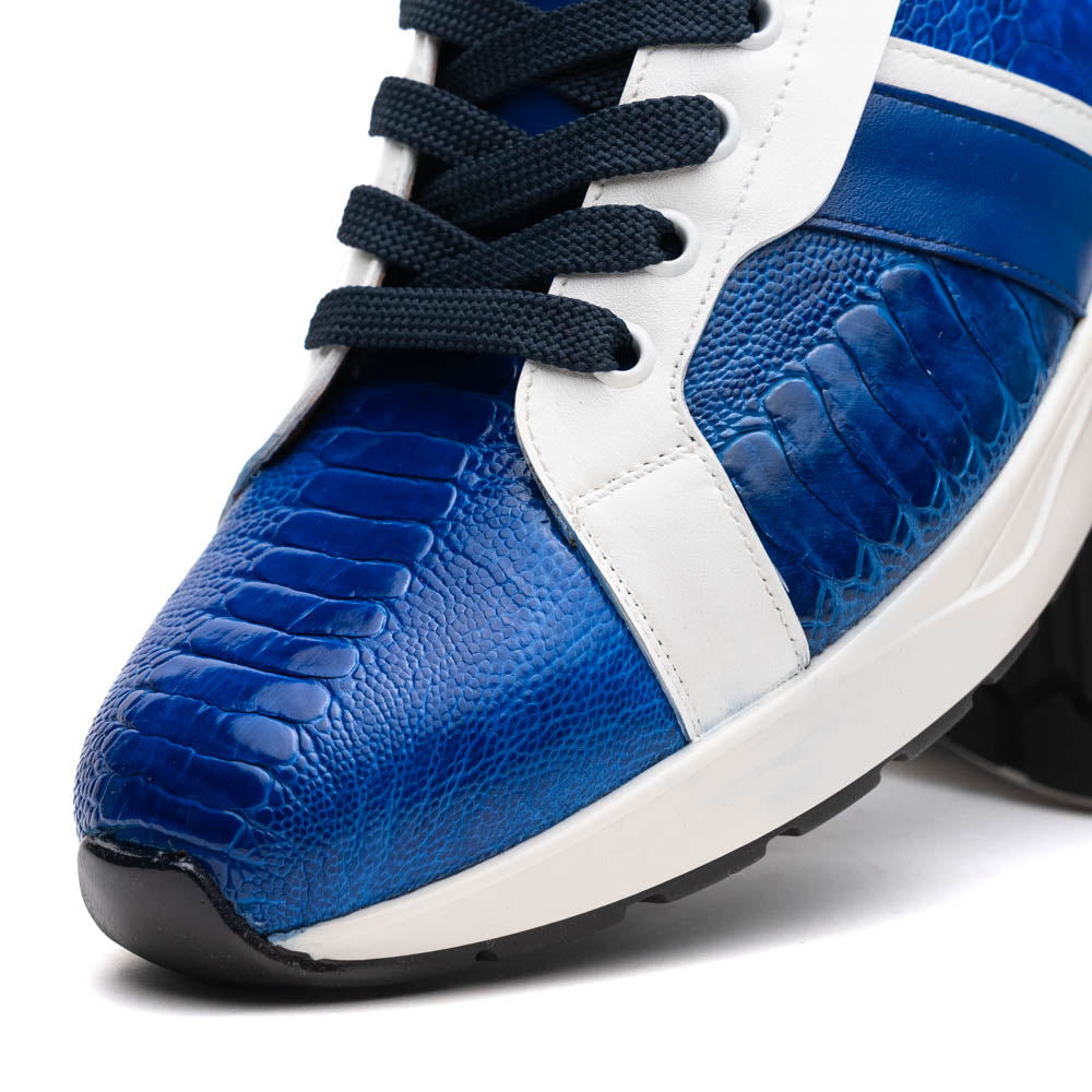 The Marco Di Milano Lyon Blue / White sneakers feature blue and white tones, black laces, textured side panels, and sleek black outsoles, with one shoe displayed stylishly on its side against the other.
