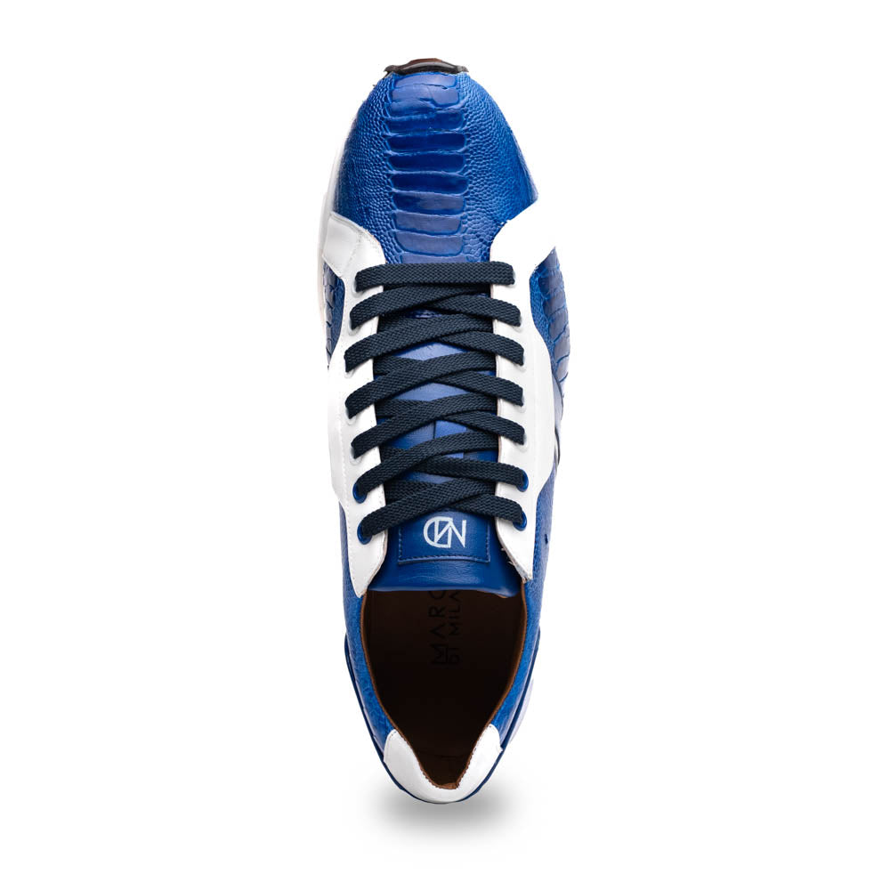 The Marco Di Milano Lyon Blue / White sneakers feature blue and white tones, black laces, textured side panels, and sleek black outsoles, with one shoe displayed stylishly on its side against the other.