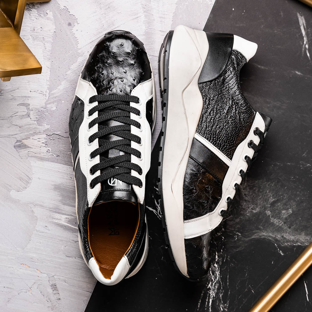 The Marco Di Milano Lyon Black / White sneakers feature a hand-painted, textured pattern, black laces, and rubber soles—one shoe shown upright, the other propped behind.