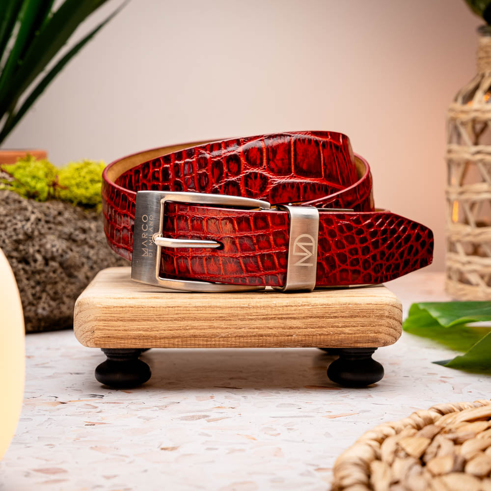 The Riccardo Belt Antique Red by Marco Di Milano is a rolled, red caiman belly belt with a crocodile pattern and a silver buckle engraved with the brand logo—an exceptional choice in luxury exotic belts.