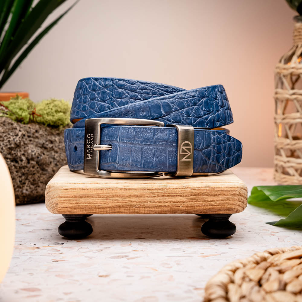 The Riccardo Belt Blue by Marco Di Milano features a caiman fuscus belly with crocodile pattern and a silver buckle engraved with "Marco Di Milano" and "MDM," making it ideal to pair with luxury footwear.