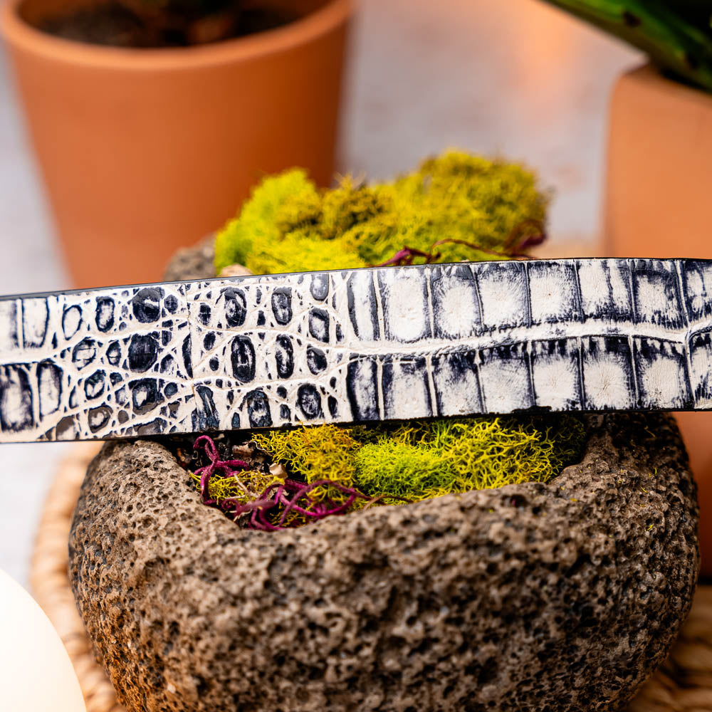 Here’s a rewritten sentence using your product data: The Silvio Belt Antique Newspaper by Marco Di Milano is a black and white genuine caiman belt with a crocodile pattern, finished with a silver buckle engraved with “Marco Di Milano.”.