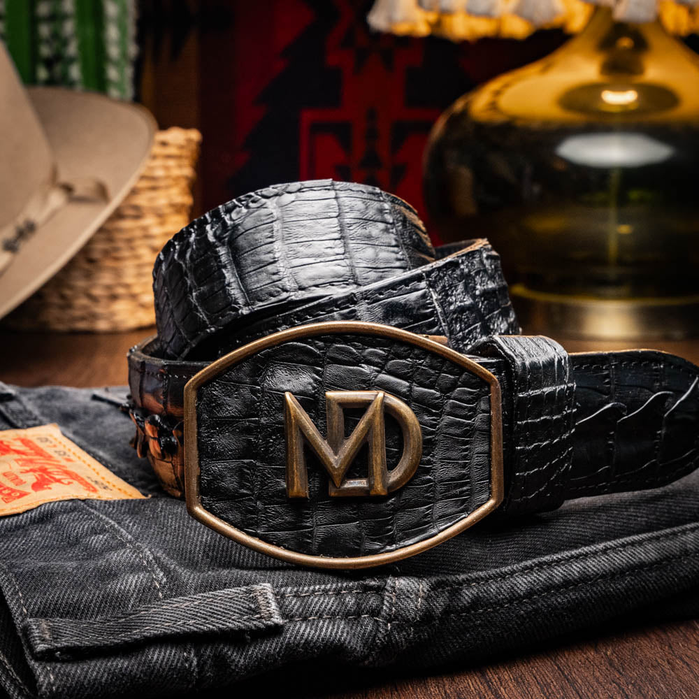 The Marlboro Belt Black by Marco Di Milano features textured hornback caiman leather and a gold buckle with stylized "MD" initials, displayed against a white background.