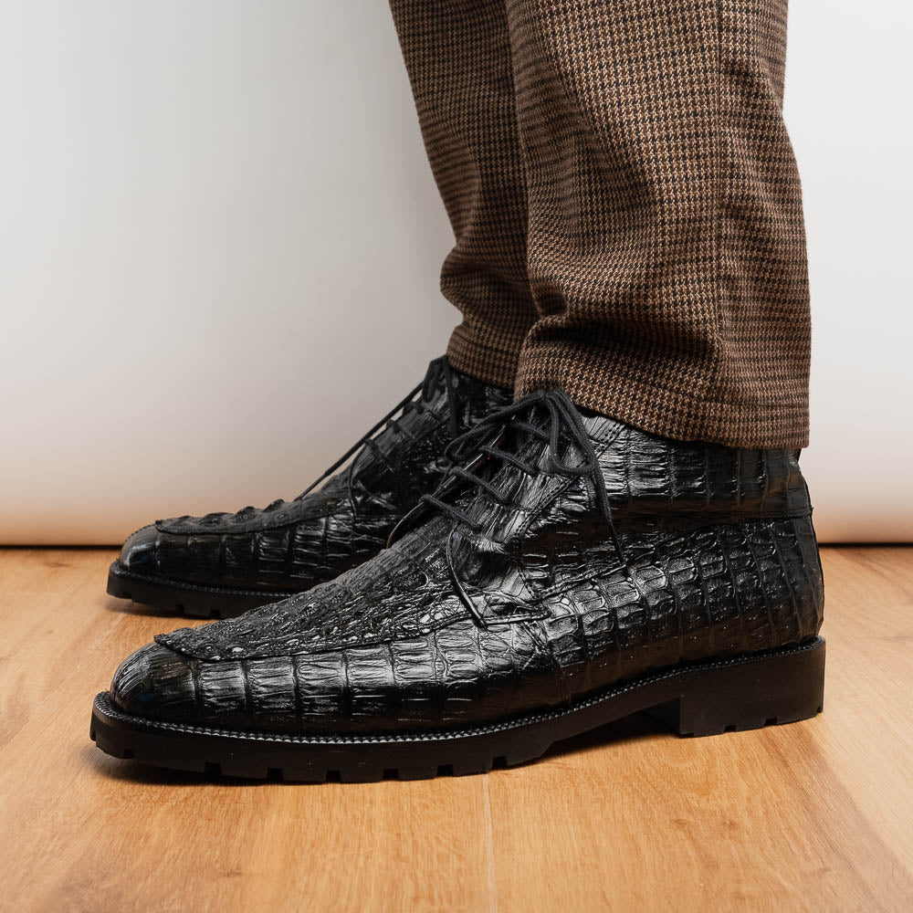The Marco Di Milano Martinelli Black boots feature crocodile-patterned leather and thick rubber soles—one upright, one sideways to show the tread—for standout men's exotic footwear.