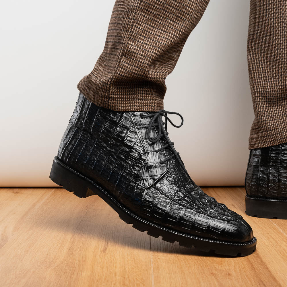 The Marco Di Milano Martinelli Black boots feature crocodile-patterned leather and thick rubber soles—one upright, one sideways to show the tread—for standout men's exotic footwear.