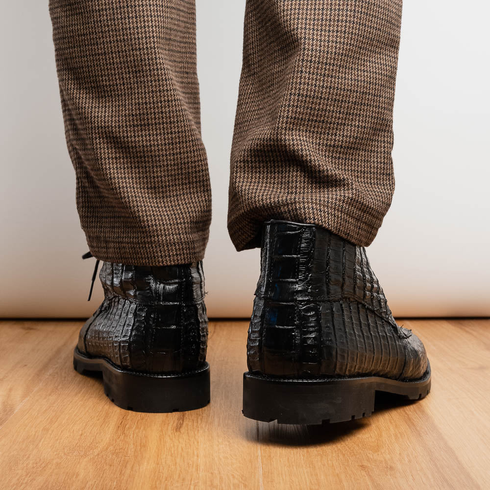 The Marco Di Milano Martinelli Black boots feature crocodile-patterned leather and thick rubber soles—one upright, one sideways to show the tread—for standout men's exotic footwear.