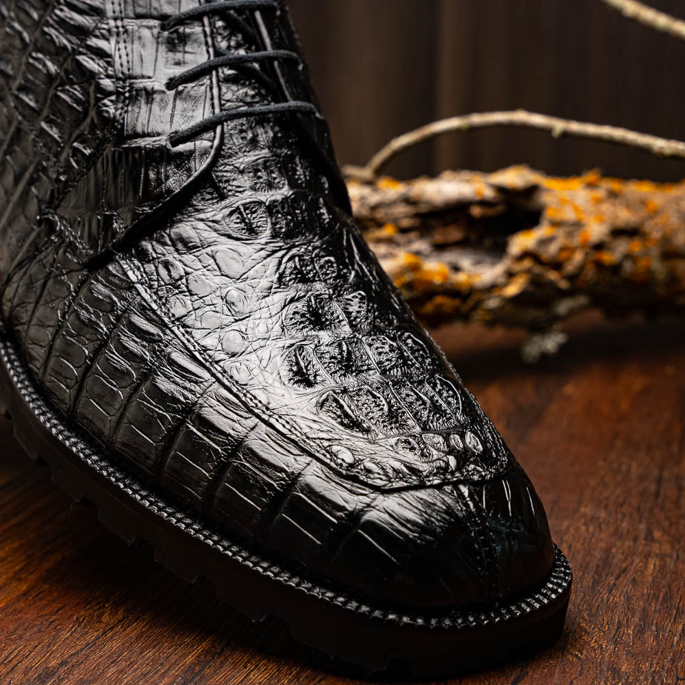 The Marco Di Milano Martinelli Black boots feature crocodile-patterned leather and thick rubber soles—one upright, one sideways to show the tread—for standout men's exotic footwear.