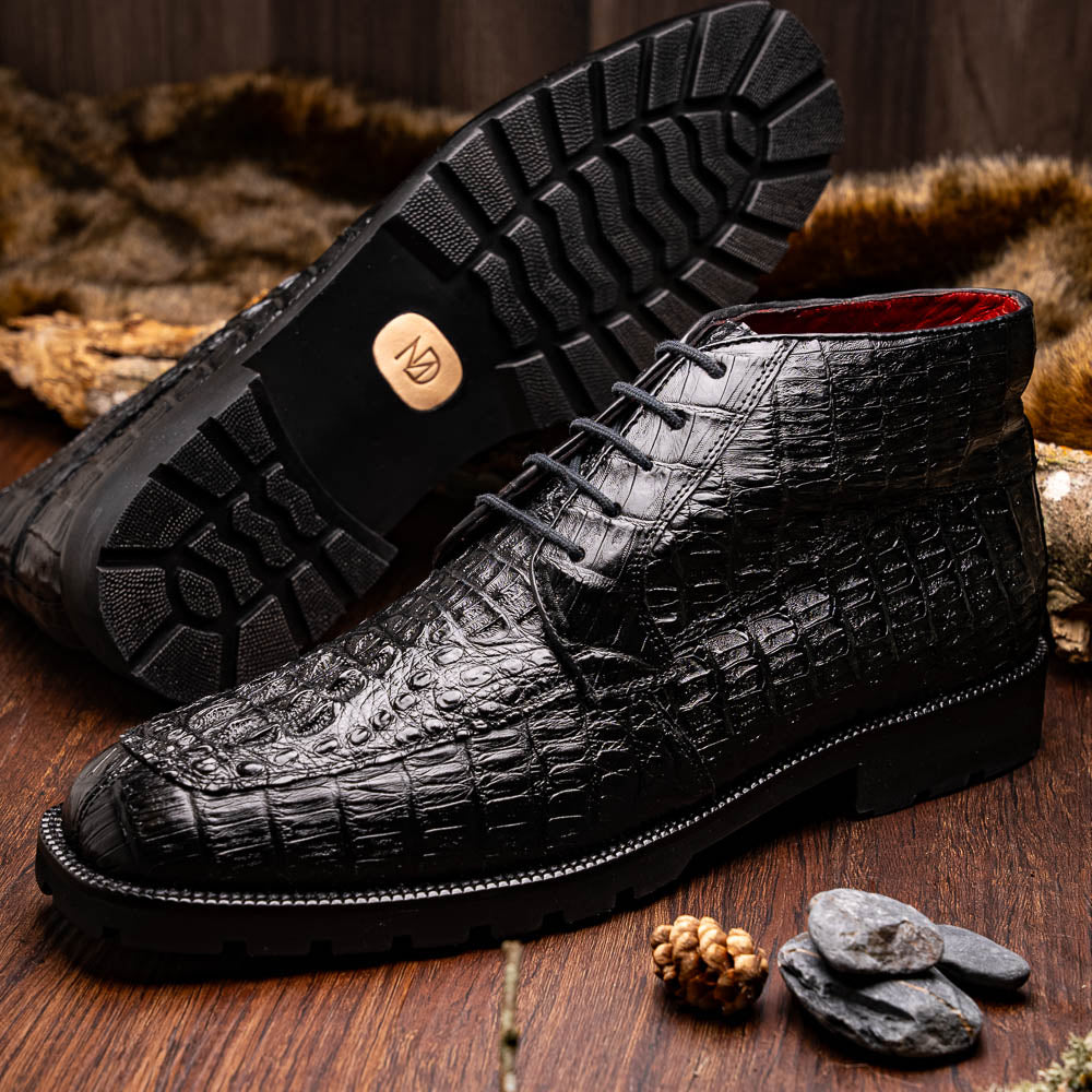 The Marco Di Milano Martinelli Black boots feature crocodile-patterned leather and thick rubber soles—one upright, one sideways to show the tread—for standout men's exotic footwear.