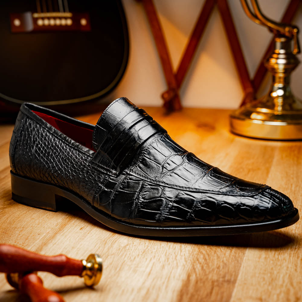 The Matteo Black by Marco Di Milano is a pair of black genuine alligator slip-on shoes with a polished brown leather sole, embossed branding, and hand-painted finishes, shown against a white background.