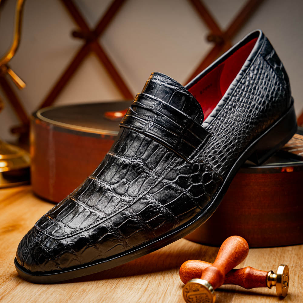 The Matteo Black by Marco Di Milano is a pair of black genuine alligator slip-on shoes with a polished brown leather sole, embossed branding, and hand-painted finishes, shown against a white background.