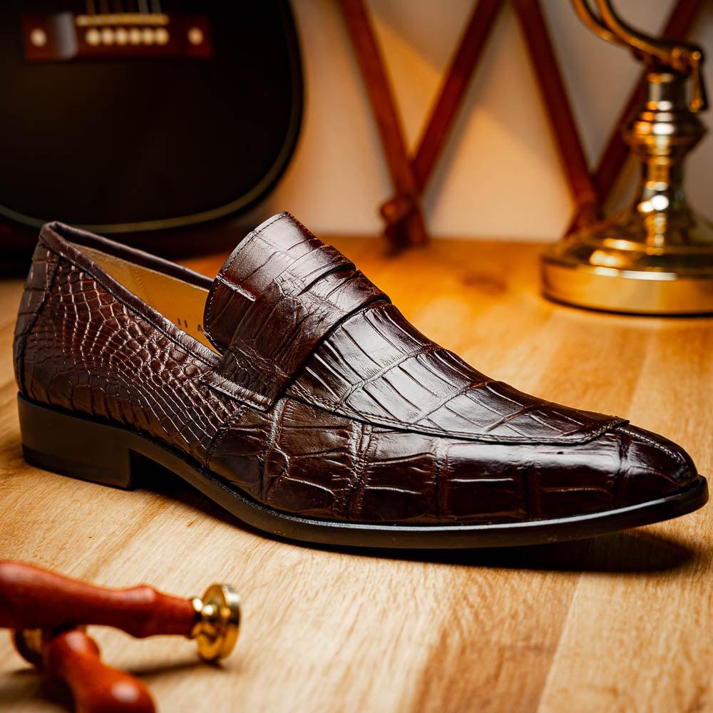 The Matteo Brown by Marco Di Milano is a pair of brown luxury loafers with a crocodile pattern; one shoe lies flat while the other is propped to showcase the sole and elegant hand-painted finishes.