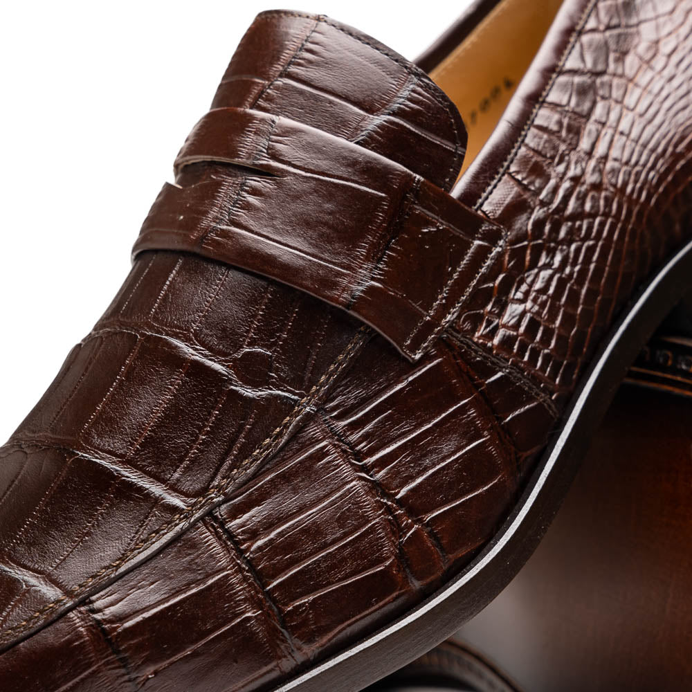 The Matteo Brown by Marco Di Milano is a pair of brown luxury loafers with a crocodile pattern; one shoe lies flat while the other is propped to showcase the sole and elegant hand-painted finishes.