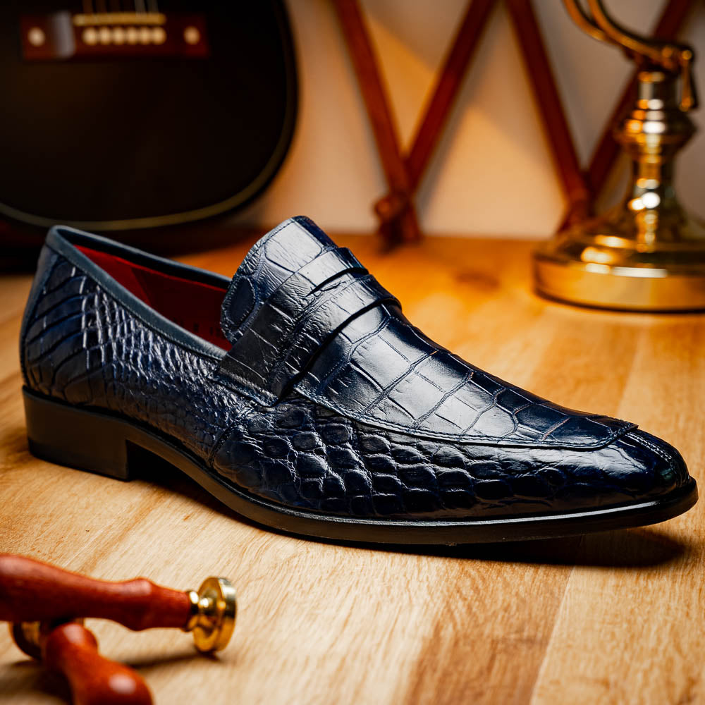 A pair of Matteo Navy loafers by Marco Di Milano, crafted in crocodile-pattern navy leather with a penny strap, red interior lining, and black soles; one shoe props against the other to reveal the sole.